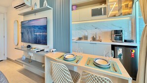 A modern kitchen with a built-in microwave, coffee machine, and refrigerator. There is a dining area with a table set for two, and a large flat-screen TV mounted on the wall. - RN Studio Premium 512 - Frente Mar (Maceio)