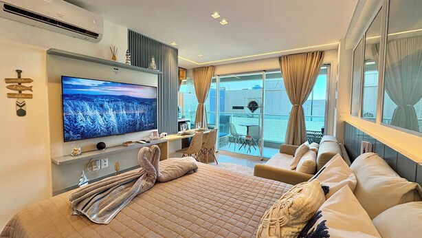 A modern hotel room with a large bed, a flat-screen TV, a balcony with a table and chairs, and a city view. - RN Studio Premium 512 - Frente Mar (Maceio)