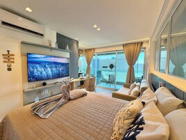 Quarto de hotel moderno com uma cama grande, televisão de tela plana, varanda com mesa e cadeiras e vista para a cidade.