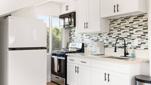 A modern kitchen with white cabinets, a stainless steel refrigerator, a microwave, a stove, and a coffee maker. - 2Bedroom home - Marengo Estate (Alhambra)