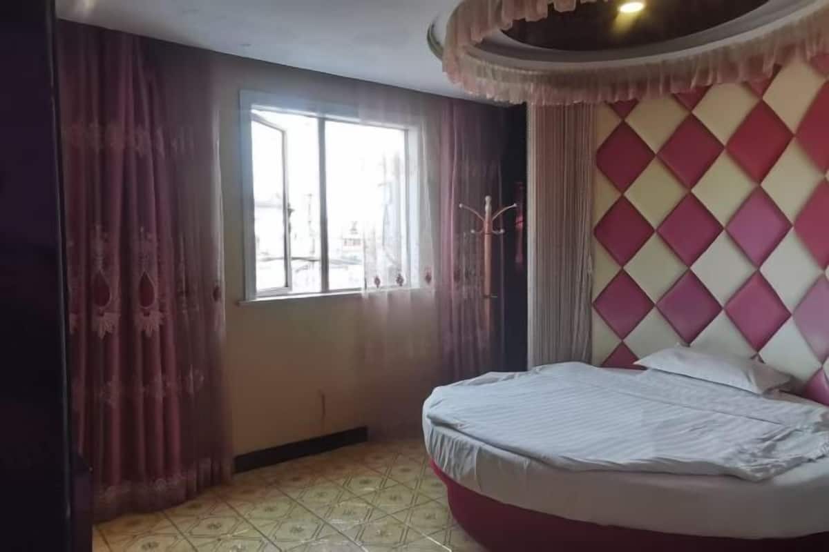 A bedroom with a bed, a window, curtains, and a patterned wall.