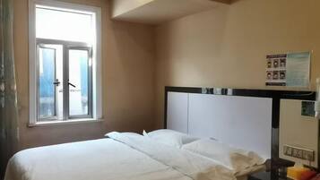 A hotel room with a bed, a window, a wall-mounted TV, and a poster on the wall.