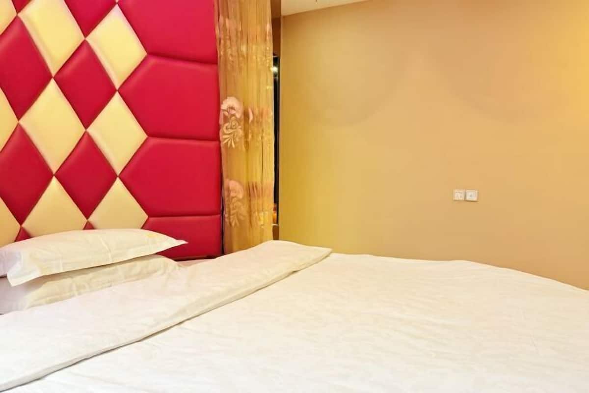 A bed with white bedding, a red and yellow headboard, and a plain wall.