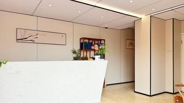 Un espace d’accueil avec un comptoir de réception blanc, une étagère en bois ornée de plantes et une œuvre d’art encadrée accrochée au mur.