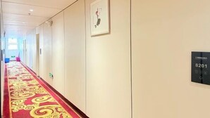 Un couloir d’hôtel avec un tapis rouge, une œuvre d’art encadrée au mur et une plaque indiquant le numéro de la chambre.