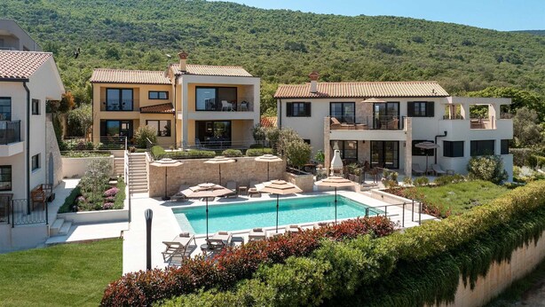 Eine moderne Villa mit Swimmingpool, Sitzgelegenheiten im Freien und Blick auf einen grünen Hügel.