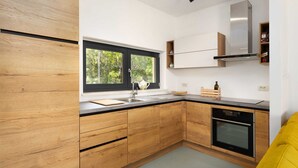 Eine moderne Küche mit Holzschränken, einer schwarzen Arbeitsplatte, einem Edelstahl-Spülbecken, einem eingebauten Ofen und einem Fenster mit Blick auf Grünflächen.