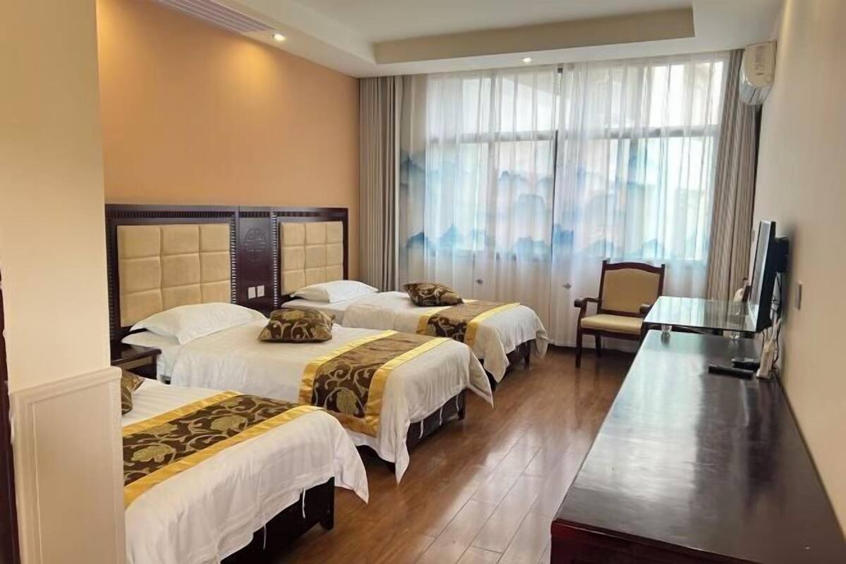 A hotel room with three beds, a wooden desk, a chair, and a TV.