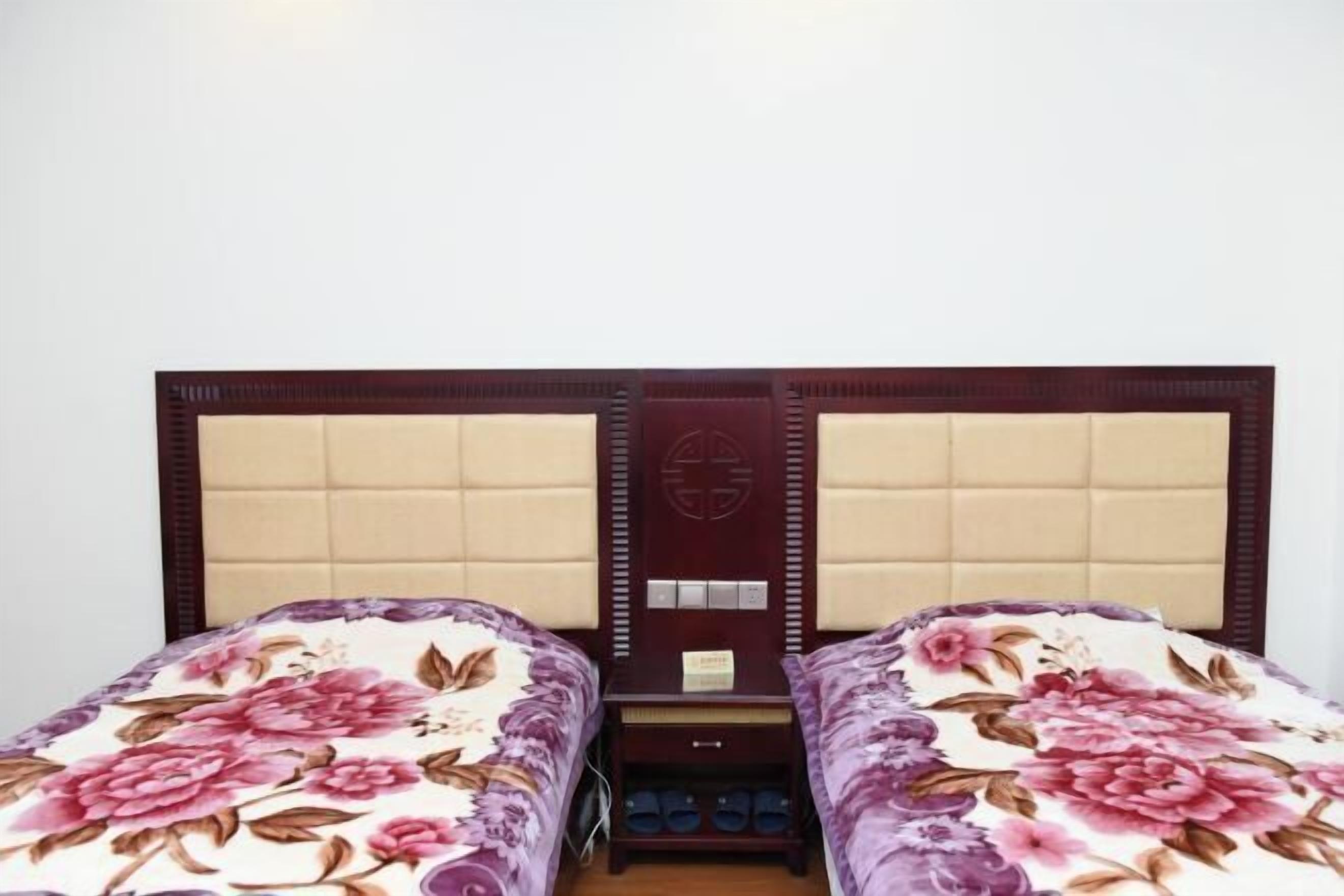 A double bed with a floral bedspread, a wooden headboard, and a small bedside table with a lamp.