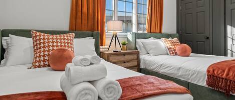 Habitación de hotel con dos camas, una mesita de noche con lámpara y vistas al exterior a través de amplias ventanas.