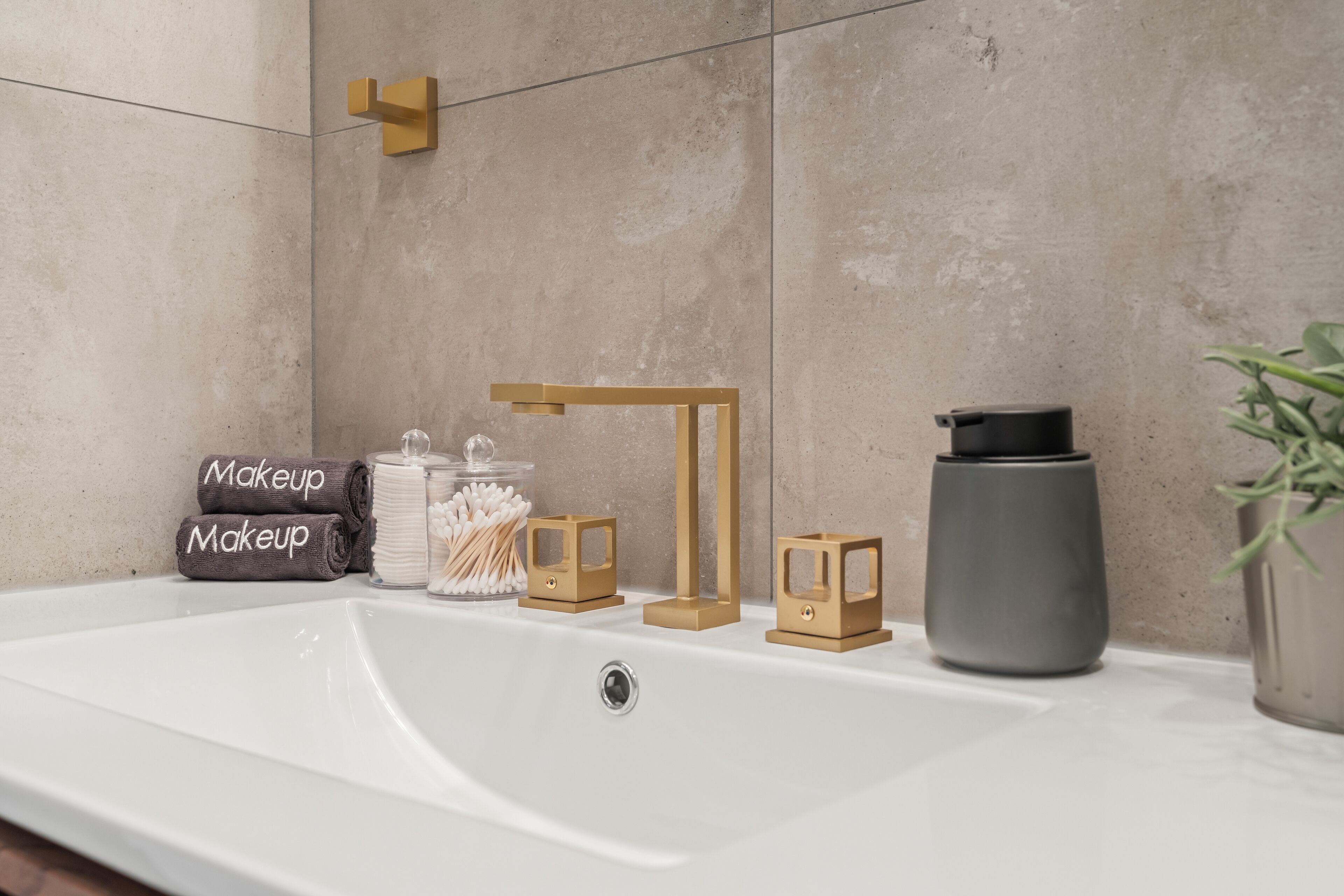 Un baño con un lavabo blanco, un perchero para toallas, un dispensador de jabón, un portacepillos de dientes y una planta en maceta.