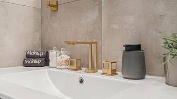 Un baño con un lavabo blanco, un perchero para toallas, un dispensador de jabón, un portacepillos de dientes y una planta en maceta.