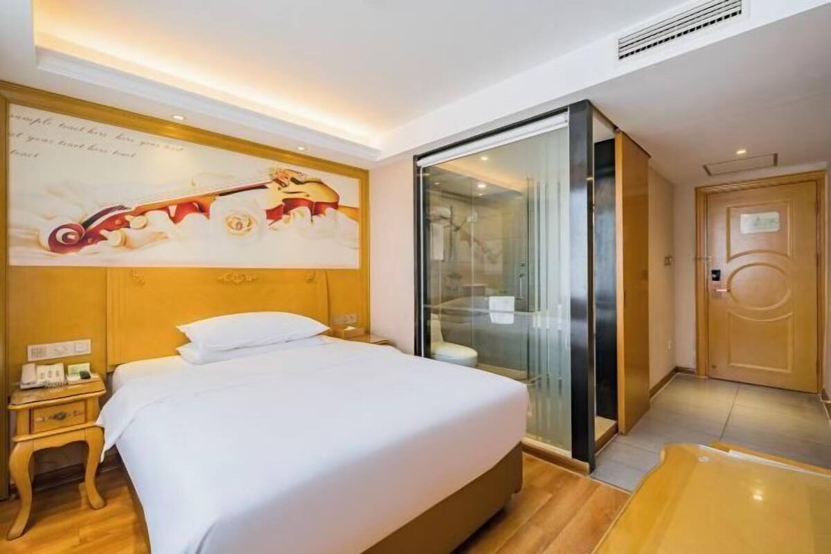 A hotel room with a bed, a nightstand, a glass-enclosed shower, and a wooden door.