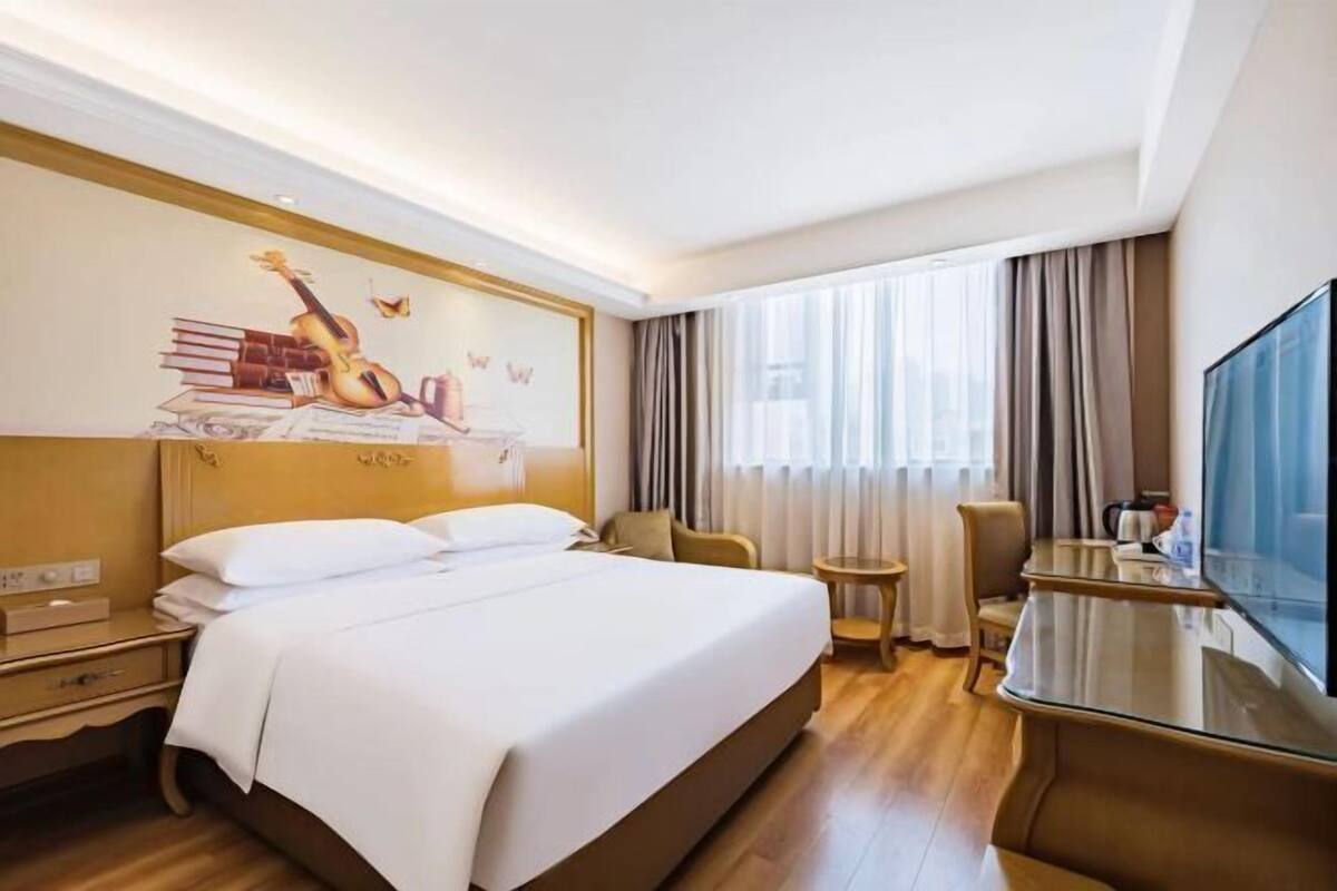 A hotel room with a large bed, a desk, a chair, and a television.
