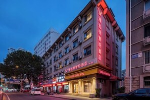 Ein mehrgeschossiges Hotel mit auffälligem rotem Schild, gut erkennbarem Eingang und Straßenansicht mit Fahrzeugen.