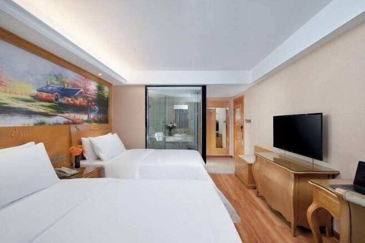 A hotel room with two beds, a TV, a desk, and a painting on the wall.