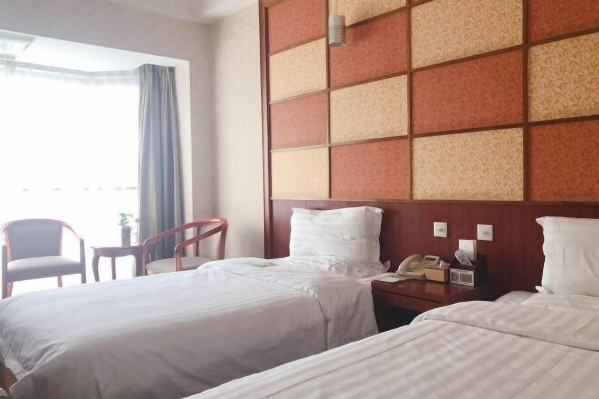 A hotel room with two beds, a wooden headboard, a nightstand with a phone, and a chair.