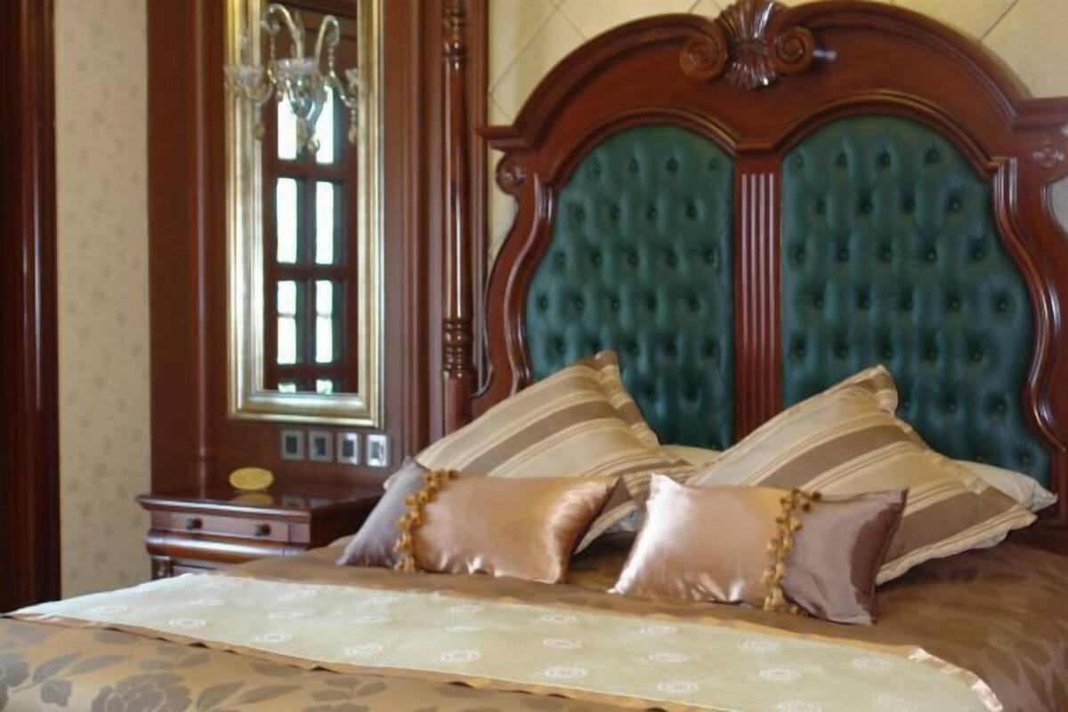 A bedroom with a tufted headboard, a bed with patterned bedding, a nightstand, and a mirror.