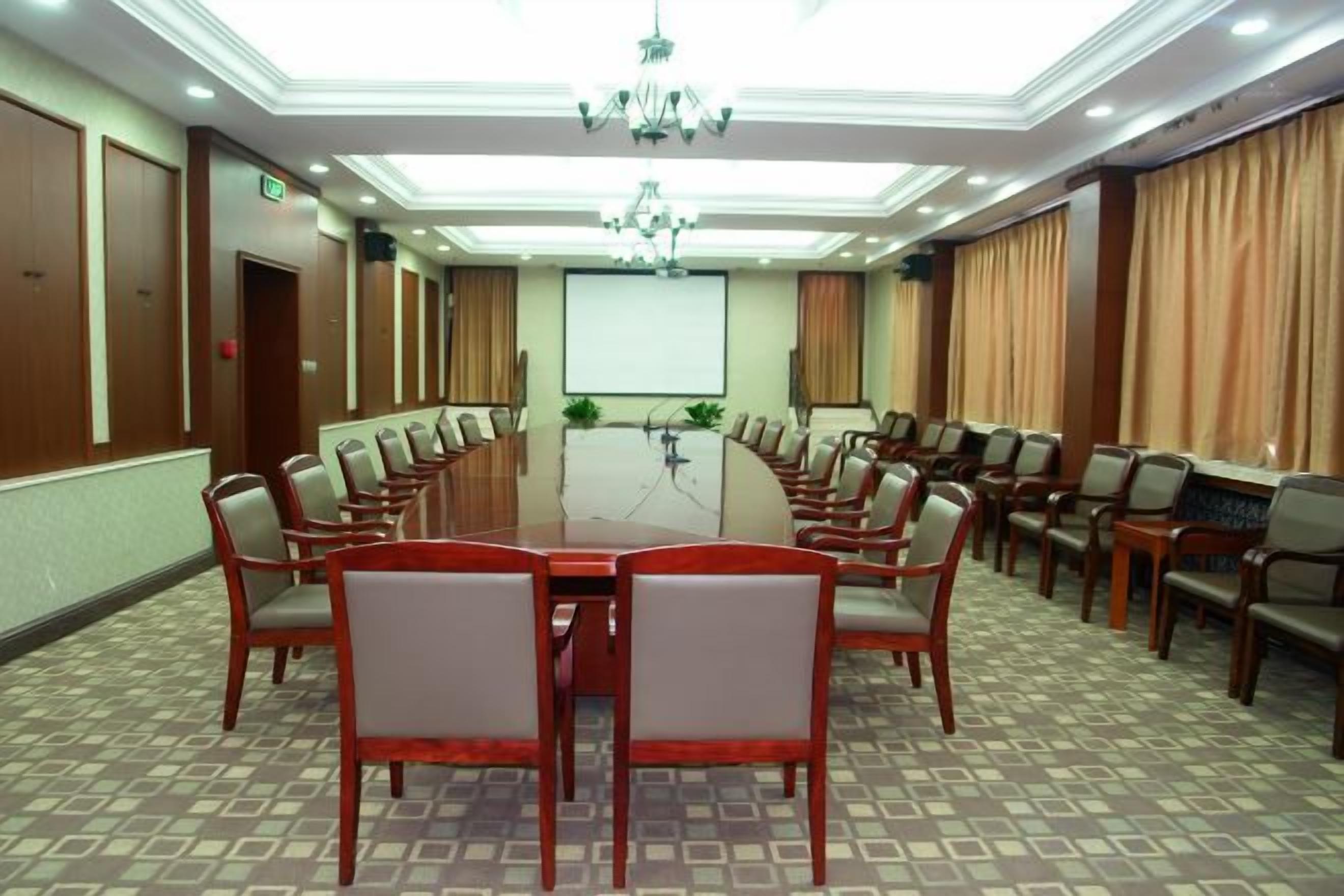 A conference room with a large oval table surrounded by chairs, a projector screen, and a chandelier.
