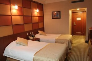 A hotel room with two beds, a wooden headboard, a bedside table with a lamp, and a framed picture on the wall.
