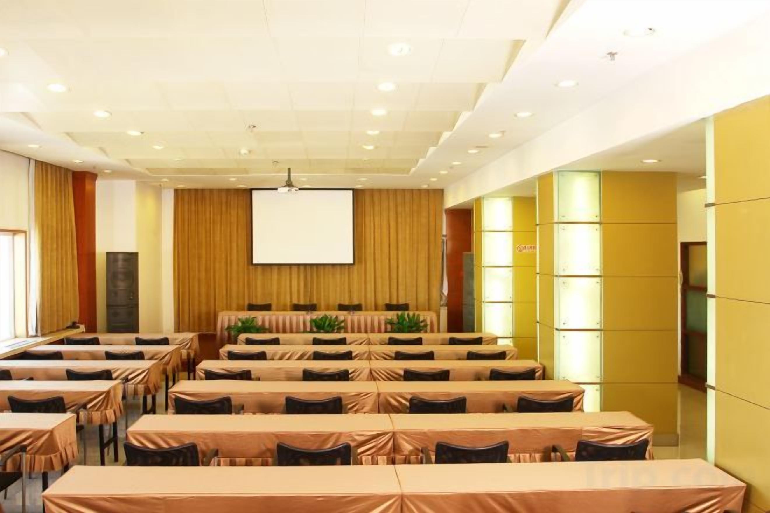A conference room with multiple tables and chairs, a large screen, and a stage area.