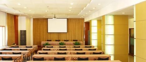 A conference room with multiple tables and chairs, a large screen, and a stage area.