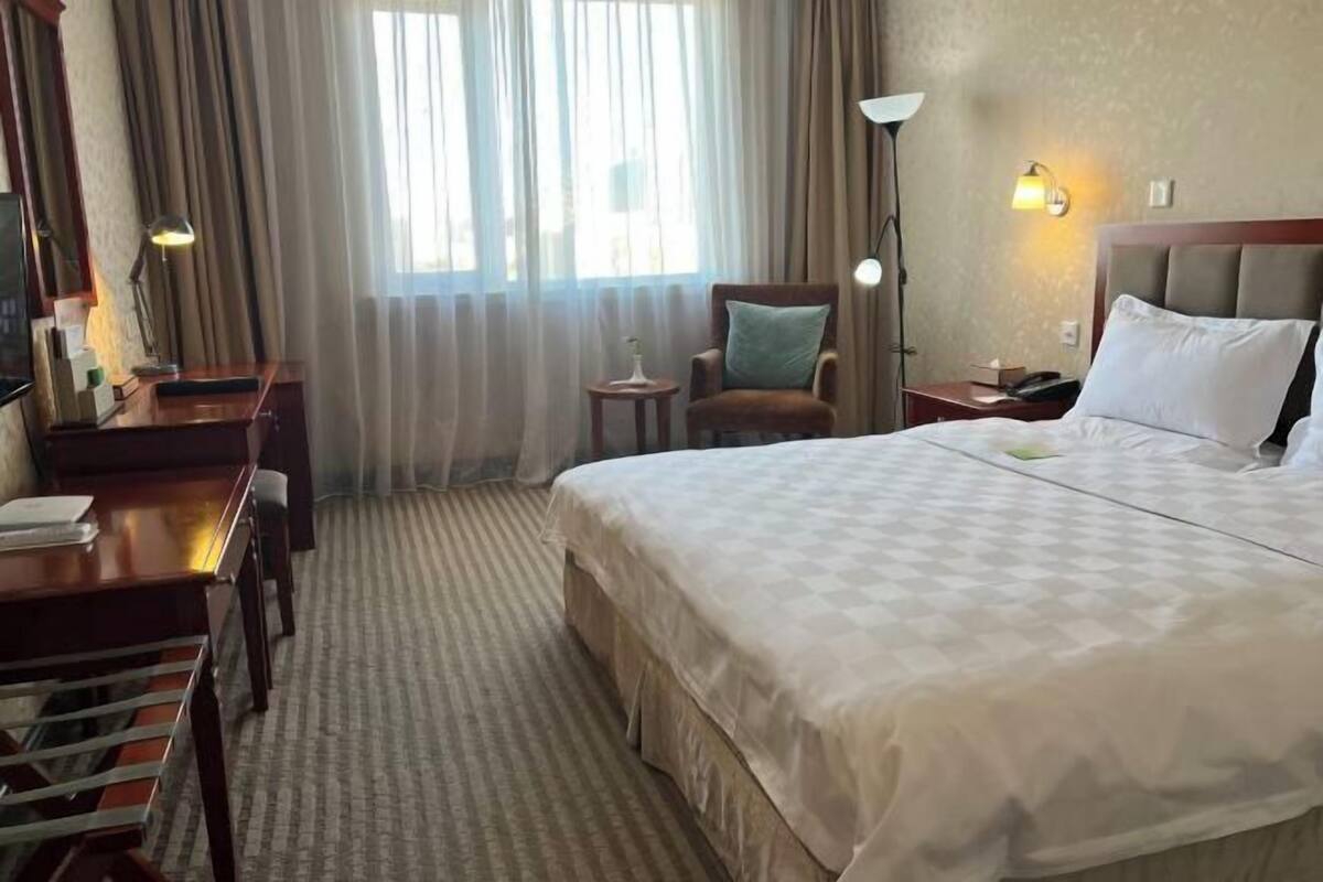 A hotel room with a large bed, a desk with a lamp, a chair, and a nightstand with a phone.