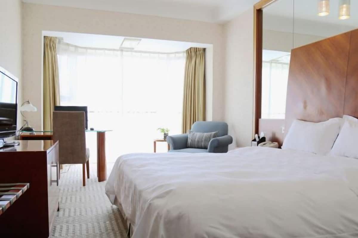 A hotel room with a bed, a desk, a chair, and a TV.