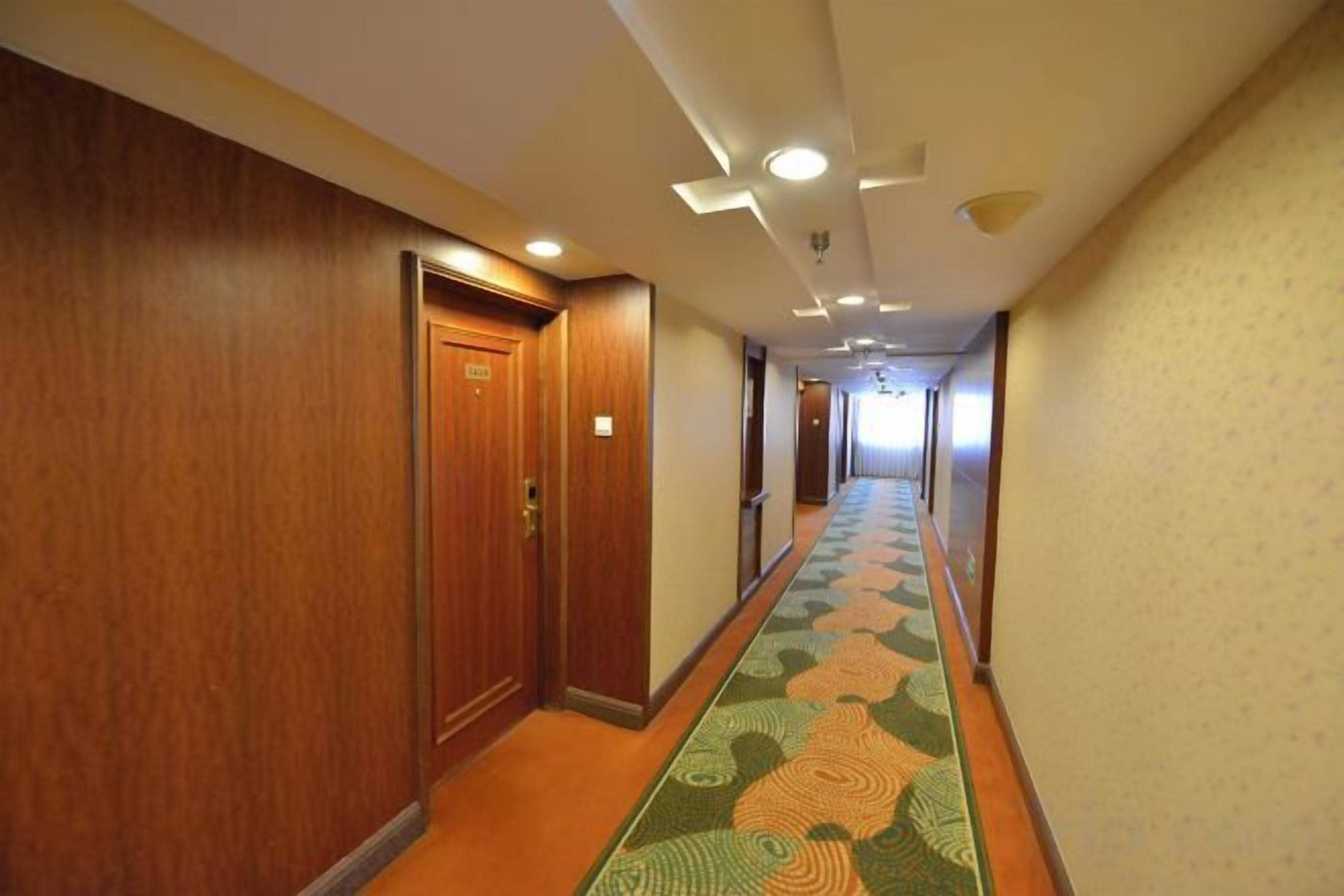 A hotel corridor with wooden doors, a patterned carpet, and recessed lighting.