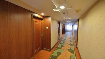 A hotel corridor with wooden doors, a patterned carpet, and recessed lighting.