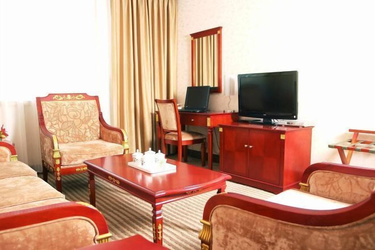 A hotel room with a TV, wooden furniture, a desk, and a chair.
