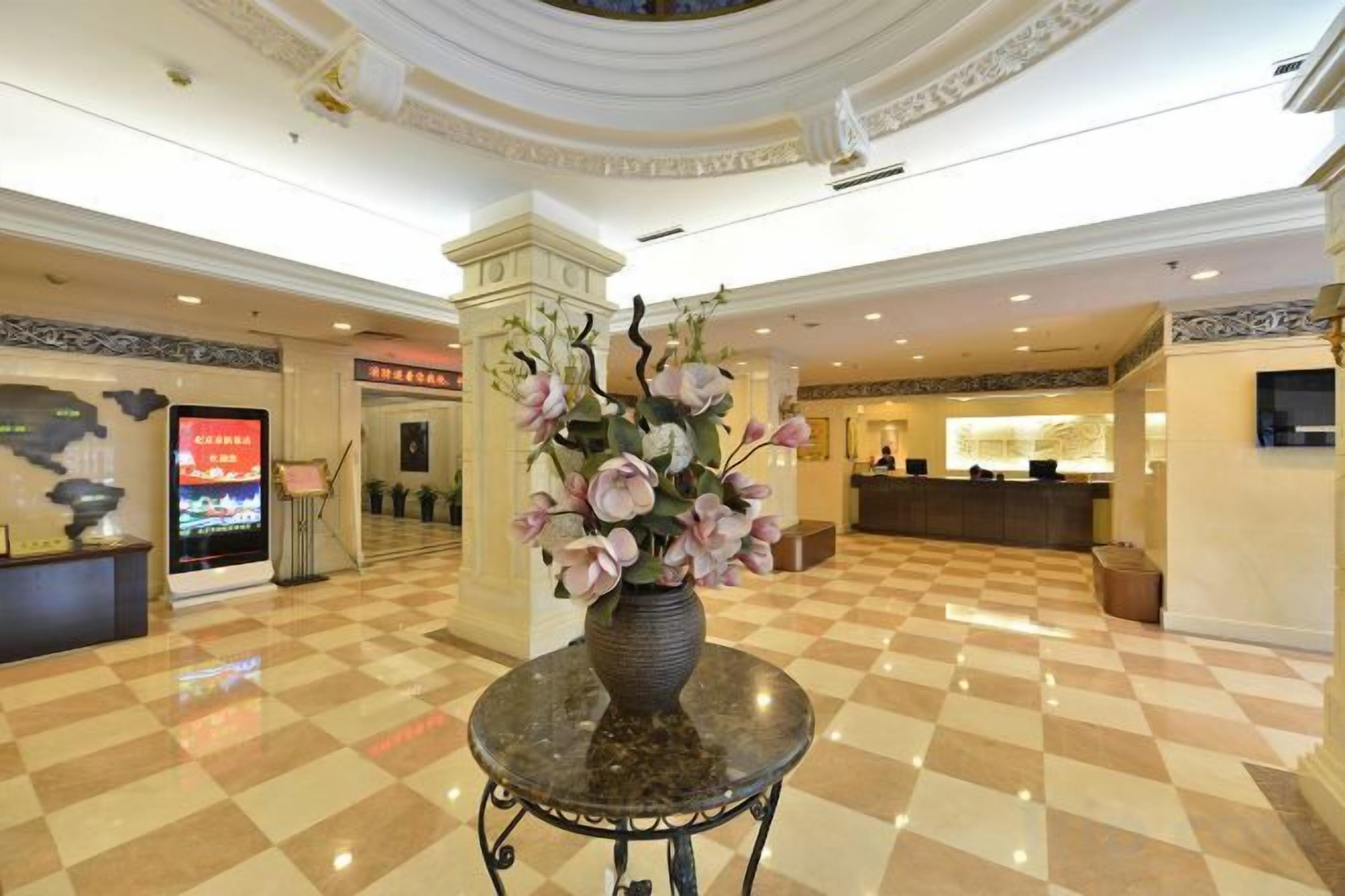 A hotel lobby with a checkered floor, a reception desk, and a decorative vase with flowers.