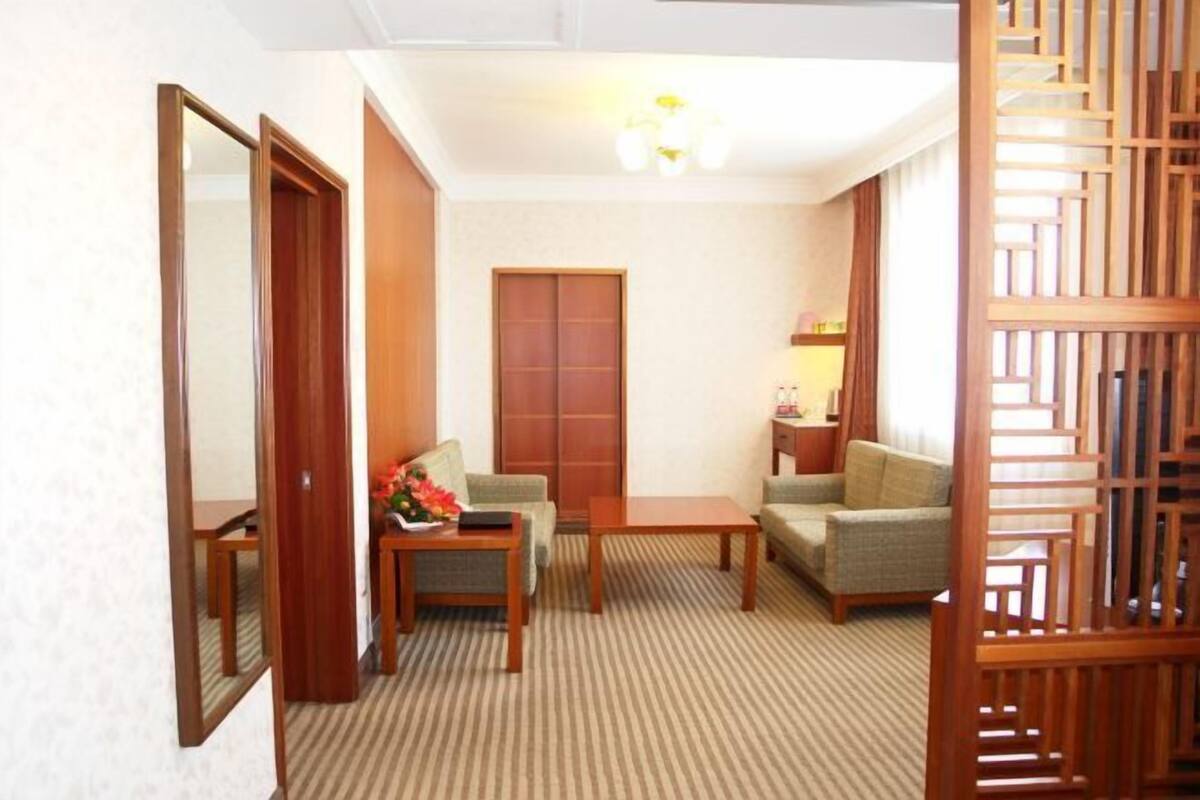 A hotel room with a wooden floor, a sofa, a small table with a vase, a cabinet, and a mirror.