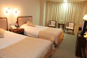 A hotel room with two beds, a desk, a chair, and a TV.
