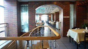 En rummelig restaurant med murstensvægge, en midterste hvælving og et spiseområde med borde og stole.