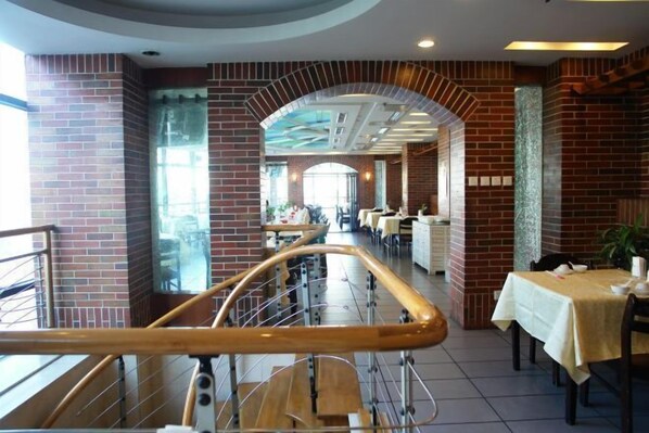 A spacious restaurant with brick walls, a central archway, and a dining area with tables and chairs. - Jingbin Hotel (Beijing)