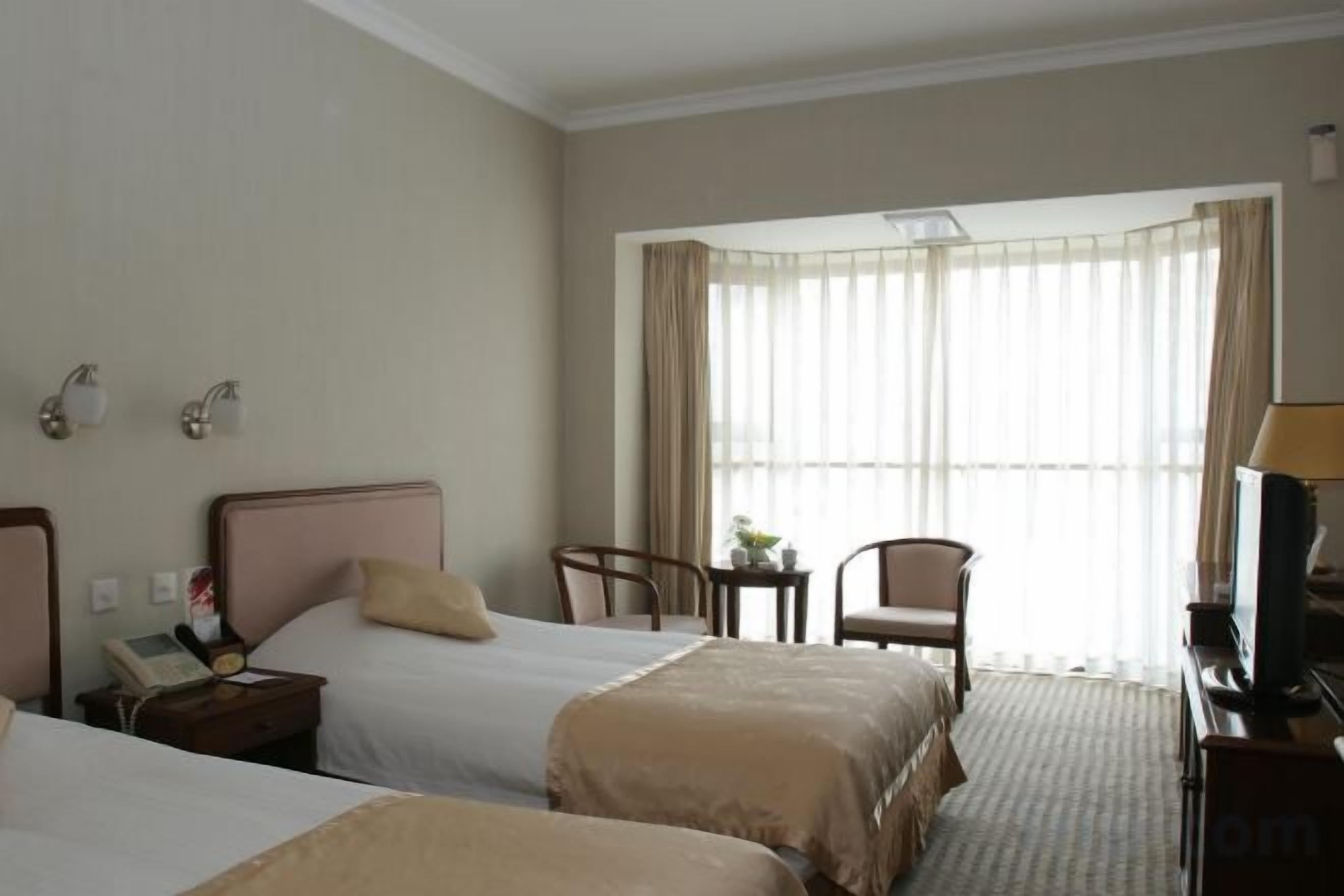 A hotel room with two beds, a desk, a chair, and a television.