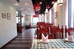 Een restaurant met een geruite tafelkleed, rode stoelen en een betegelde vloer.