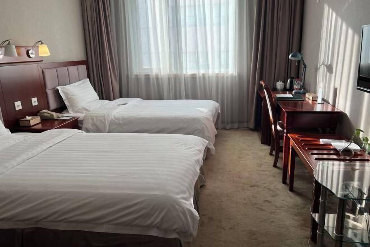 A hotel room with two beds, a desk, a chair, a TV, and a window with curtains.
