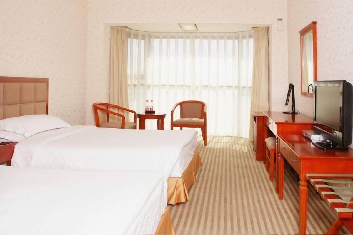 A hotel room with a bed, a desk with a television, a chair, and a window with curtains.