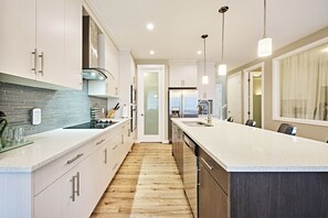 Une cuisine moderne dotée d’un îlot central, d’appareils électroménagers en acier inoxydable et de luminaires suspendus.