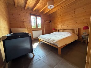 Ein Zimmer einer Holzhütte mit einem Bett, einem Heizgerät, einem Heizkörper und einem kleinen Tisch mit einer Lampe.