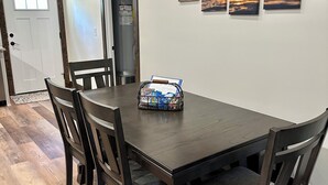 A dining area with a dark wooden table and chairs, a small basket of snacks, and a door leading to another room. - Rayburn Blue•Close to Ramp•New Home•Large Driveway for Multiple Trucks and Boats (Zavalla)