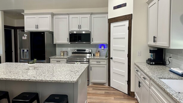 A modern kitchen with white cabinets, a granite countertop, stainless steel appliances, and a central island with stools. - Rayburn Blue•Close to Ramp•New Home•Large Driveway for Multiple Trucks and Boats (Zavalla)