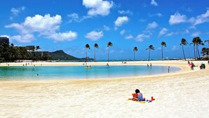 Une plage avec une eau d’un bleu limpide, des palmiers et quelques personnes.