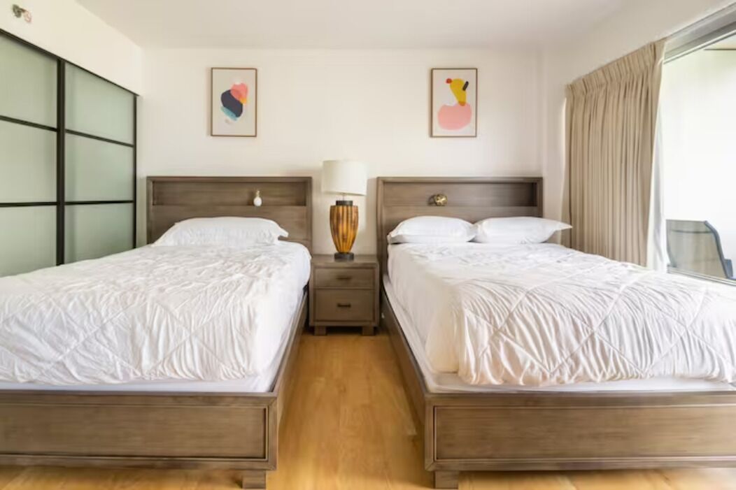 A hotel room with two beds, a nightstand with a lamp, and artwork on the walls.