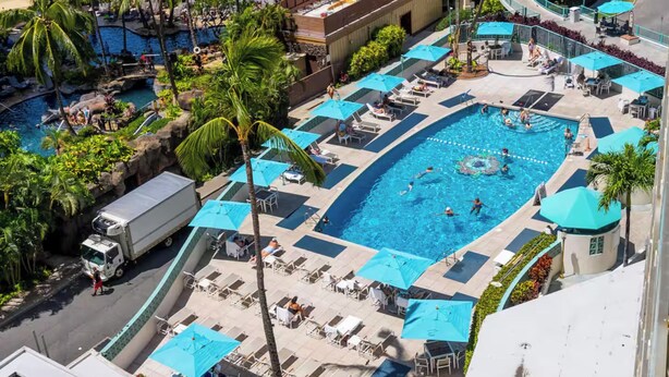 Un espace piscine sur le toit, comprenant plusieurs piscines, des chaises longues et des parasols.