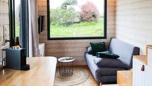 Interior acogedor de una cabaña con un ventanal grande, paredes de madera, un sofá, una mesita y un televisor.