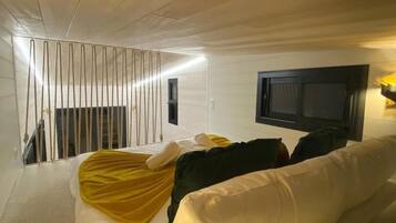Ein modernes Hotelzimmer mit einem weißen Sofa, einem flachbildfernseher an der Wand und einer Treppe, die in eine höhere Ebene führt.