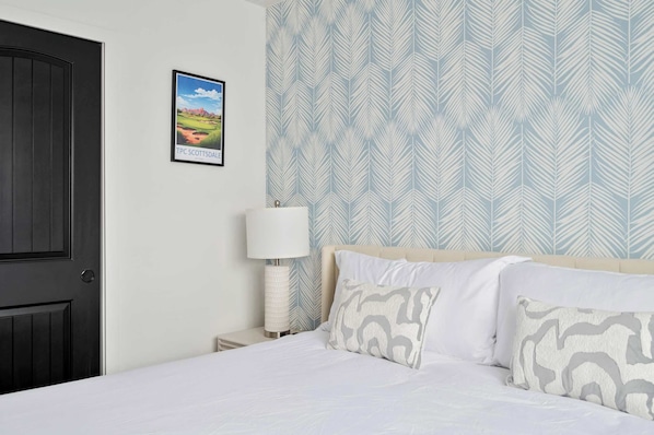 Een slaapkamer met een bed, nachtkastje, lamp en een ingelijst schilderij aan de muur.